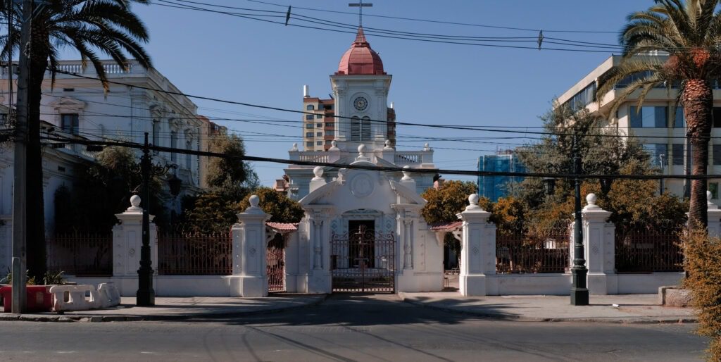 Frontis actual de la Iglesia Santa Lucrecia. En el centro se observa la cúpula de la parroquia. A los costados están el ala izquierda y derecha de la parroquia con dos ventanas cada una. En frente de la edificación se encuentra una pileta de mármol y la iglesia está flanqueada por dos palmeras.